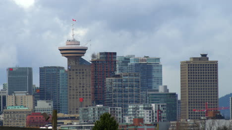 Horizonte-Urbano-De-Vancouver-Con-Torre-Y-Ondeando-La-Bandera-Canadiense,-Mientras-El-Tren-Aéreo-Público-Pasa-Y-Conduce-En-Dirección-Al-Centro