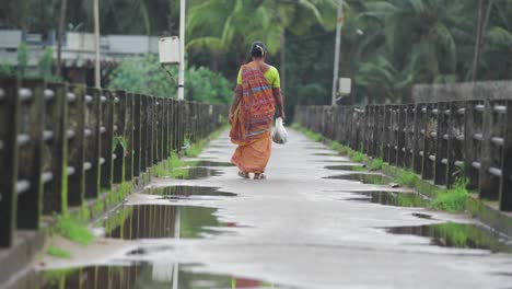Tiro-Inclinado-Que-Muestra-A-Una-Mujer-India-En-Sari-Tradicional-Caminando-Por-El-Camino-Después-De-La-Lluvia-En-India