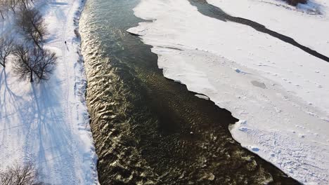 Frozen-winter-river-with-streaming-water-in-high-angle-drone-shot