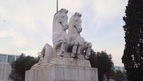Statue-of-two-horses-with-building-and-bird-flying-in-the-background