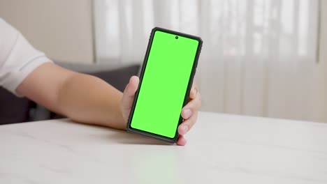 Die-Hand-Des-Mannes-Zeigt-Ein-Mobiles-Smartphone-Mit-Grünem-Bildschirm-In-Vertikaler-Position-Isoliert-Auf-Grünem-Hintergrund