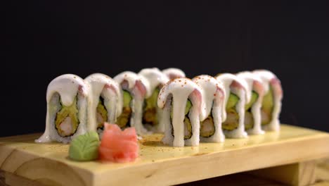 Sushi-Roll-with-sauce-on-top-being-sprinkled-with-red-toppings,-served-on-a-wooden-japanese-plate