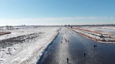People-ice-skating-on-frozen-canals-in-Netherlands,-4K-winter-aerial-view