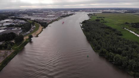Luftaufnahme-über-Dem-Fluss-Mit-Trivor-Binnentanker-In-Der-Ferne-In-Den-Niederlanden