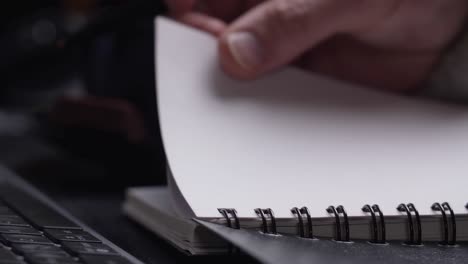 Close-up-of-man's-hands-writing-in-spiral-notepad-placed-on-wooden-black-desktop