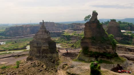 Passing-two-rock-columns-to-reveal-aerial-panorama-of-Brown-Canyon-quarry,-Java
