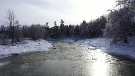Winterszene-Mit-Schönem-Schnee-Auf-Bäumen,-Niedrige-Luftaufnahme-Entlang-Des-Halb-Zugefrorenen-Flusses