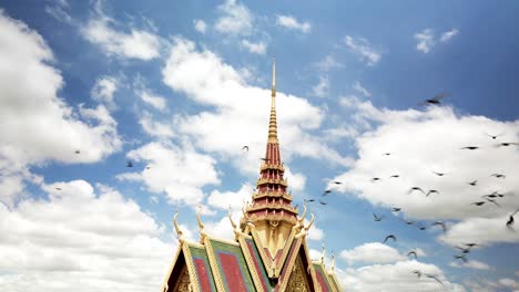 Birds-flying-to-freedom-slow-mo-around-peaceful-buddhist-pagoda-spire-with-beautiful-blue-sky-and-fluffy-clouds,-simple-clean-slow-drone-rotate-orbit