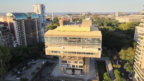 Aerial-lowering-on-Buenos-Aires-National-Library-between-trees-and-buildings-near-Rio-de-la-Plata-at-sunset