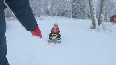 Hand-Pulling-A-Sled-On-Snow-With-Son-Riding-At-Winter-In-Sweden