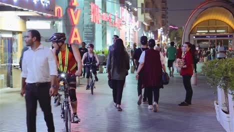 Trabajadoras-Distribuyendo-Folletos-Sobre-Lugareños-Y-Turistas-Caminando-En-La-Acera-Por-La-Noche-En-La-Ciudad-De-Dubai,-Emiratos-árabes-Unidos