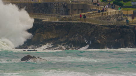 People-watching-massive-ocean-waves-hit-rocky-coastline,-static-shot