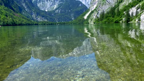 Tilt-up-of-crystal-clear-mountain-lake-during-summertime-with-blue-sky-and-green-shoreline---Obersee-Germany-in-Summer