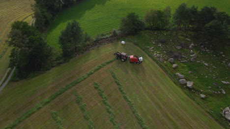 Tractor-with-baling-machine-making-silage-bales-on-farmland,-ascending-shot