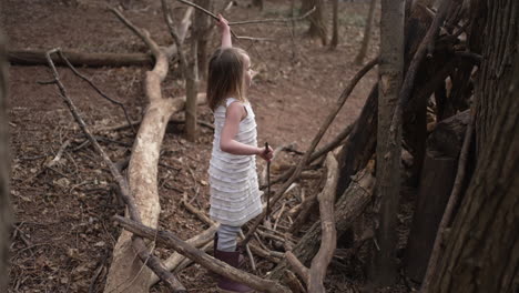 Little-girl-building-a-stick-fort-in-a-forest,-slow-motion