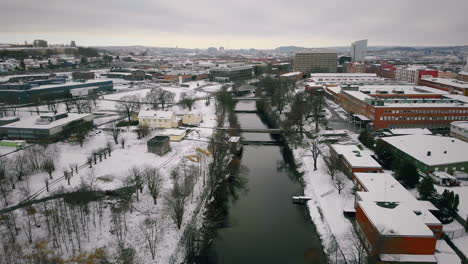 Aerial-view-of-industrial-area-crossed-by-the-river-after-first-snowfall,-Sweden