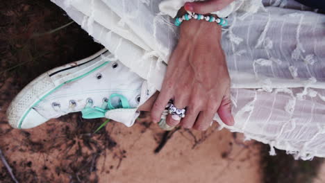 Closeup-view-of-female-hands-as-they-run-over-white-shoes,-sitting-on-the-grass-and-wearing-a-white-dress