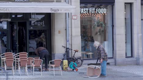 Hombres-Limpiando-Sillas-Fuera-Del-Café-Y-Preparándose-Para-Reabrir-Debido-Al-Bloqueo-Pandémico-En-Grote-Markt,-Lovaina,-Bélgica