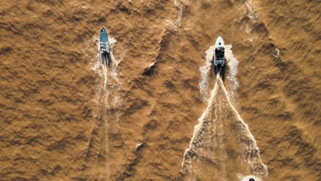 Aerial-top-down-of-a-group-of-yachts-sailing-on-a-brown-color-river-at-daytime