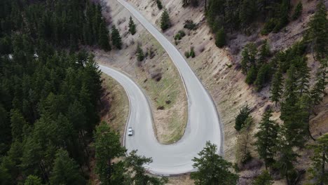 Aerial-view-of-car-driving-on-road-through-a-forest-in-British-Columbia,-Canada