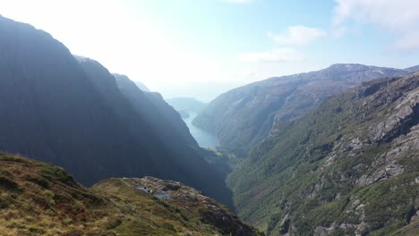 Beautiful-woman-standing-on-top-of-cliff-surrounded-by-dramatic-landscapes-and-complete-wilderness-in-Norway-mountains---Aerial-close-to-person-at-Kiellandbu-Norway