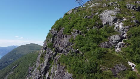 Via-Ferrata-hiking-path-along-the-edge-of-cliff-Hoven---Including-view-of-popular-risky-basejumping-spot---Upward-moving-aerial-against-top-of-mountain-Hoven-and-Loen-Skylift---Nordfjord-Norway