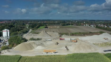 Movement-at-a-sand-pit,-trucks-and-an-excavator-are-working-at-a-beatuiful-day-in-summer-under-a-blue-cloudy-sky