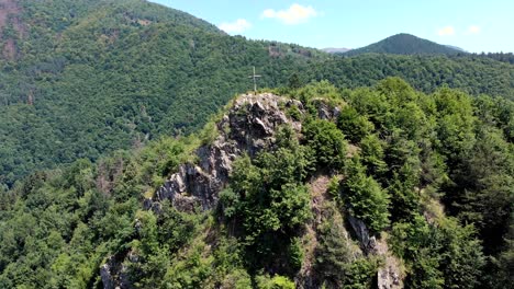 Summit-Cross-At-The-Rocky-Cliff-And-Green-Forest-Covered-The-Mountain-Range