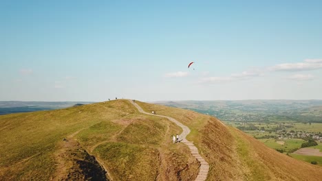 Aerial-drone-shot-of-people-on-top-of-Mam-Tor,-Castleton,-Peak-District-and-following-a-paraglider