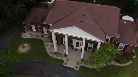 Aerial-Drone-Footage-Panning-Up-to-a-Large-House-with-Columns-and-Landscaping-in-a-Luxury-Neighborhood