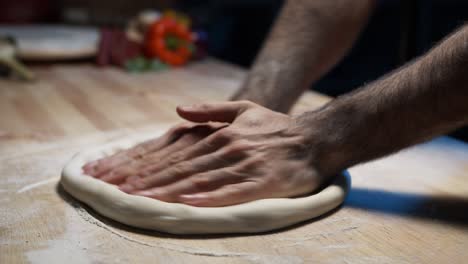 Eine-Nahaufnahme-Der-Hände-Eines-Erfahrenen-Kochs,-Der-Pizzateig-Auf-Der-Holztheke-Drückt-Und-Flach-Macht