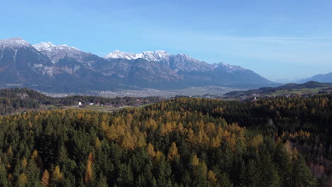 Vuelo-Aéreo-Sobre-Bosques-De-Coníferas-En-El-Valle-De-Innsbruck,-Alpes-En-Segundo-Plano.