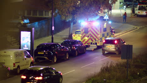 A-London-bus-drives-past-an-ambulance-with-flashing-lights-at-night,-England