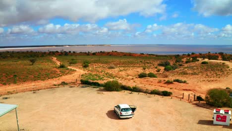 Aerial-view-of-a-car-in-a-parking-aeria-in-Australian-outback-with-a-lake-in-the-background---Victoria,-Australia