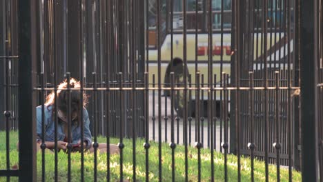 young-girl-wearing-mask-using-phone-in-the-park-surrounded-by-fence