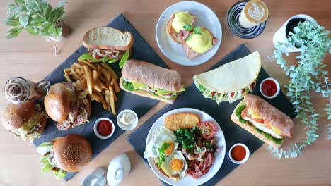 Cafe-latte-pushed-into-frame-next-to-brunch-flat-lay-with-sandwiches,-burger-and-chips