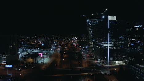 Night-time-aerial-over-dark-highway-in-urban-city-with-towers,-4K