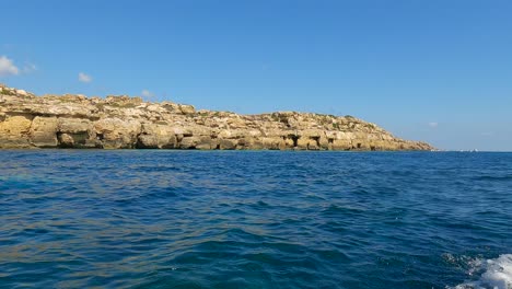 Low-angle-sea-level-view-from-cruising-boat-of-Favignana-island-coastline-and-turquoise-sea-water-in-Sicily,-Italy
