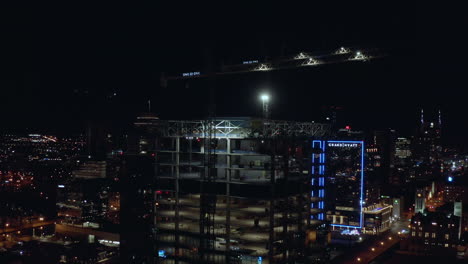 Night-city-aerial-of-building-tower-under-construction-with-cranes-on-top,-4K