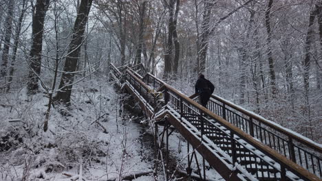 Wide-shot-of-a-jogger-climbing-a-snow-covered-stairwell-in-a-forest