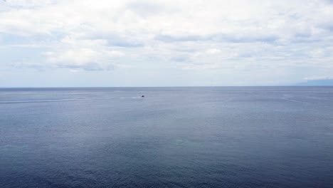 Dive-motorboat-moving-quickly-along-the-horizon-from-left-to-right-over-coral-reef-on-tropical-island-destination,-static-aerial-drone-of-ocean,-boat-and-reefs