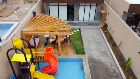 Drone-shot-of-a-house-backyard-with-a-pool-and-water-slides,-reverse-dolly-tilt