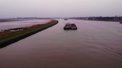 Aerial-Flying-Over-Of-Maas-Cargo-Ship-Paired-With-Another-Carrying-Containers-On-River-Noord-Beside-Crezeepolder-On-Cloudy-Afternoon