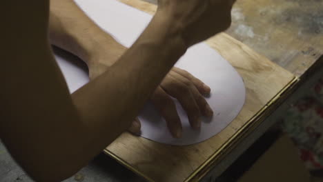 Hands-of-man-outlining-shape-of-a-DIY-skateboard-project-on-wooden-plank