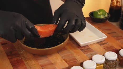Faceless-chef-wearing-black-gloves,-marinating-salmon-fish-fillet-with-citrus-ponzu-sauce-prior-to-cooking,-adding-extra-flavor-and-soften-the-texture-of-the-fish