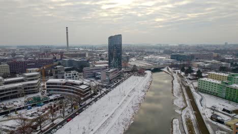 Aerial-drone-shot-over-snow-covered-Olomouc-city-in-Moravia-region-of-Czech-Republic-with-beautiful-modern-buildings-and-bridge-over-the-river-passing-by-on-chilly-winter-evening