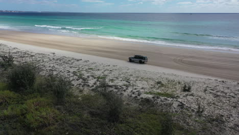 Aerial-slowly-orbits-truck-driving-on-expansive-Australian-sandy-beach