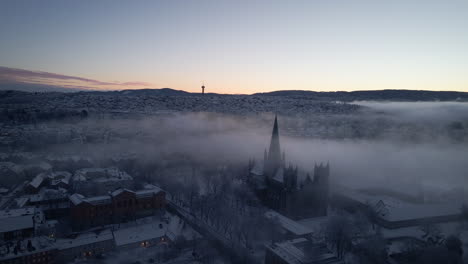 Nidaros-Cathedral-Shrouded-In-Mist-During-Winter-In-Trondheim,-Norway---aerial-drone-shot