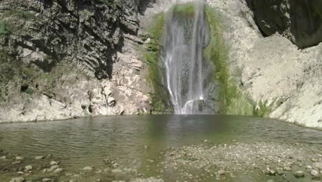 Junger-Wanderer-Sitzt-über-Einem-Stein-In-Einer-Atemberaubenden-Berglandschaft-Mit-Einem-Unberührten-Wasserfall