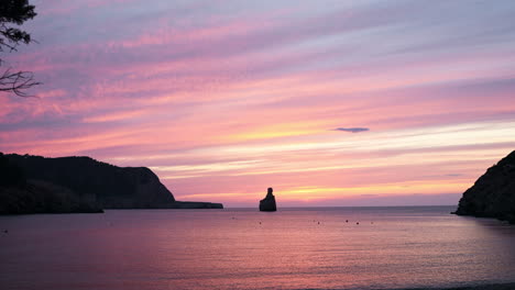 Beautiful-sunrise-pink-sky-over-beach,-Benirras,-Ibiza,-Spain,-wide-shot-tilt-up